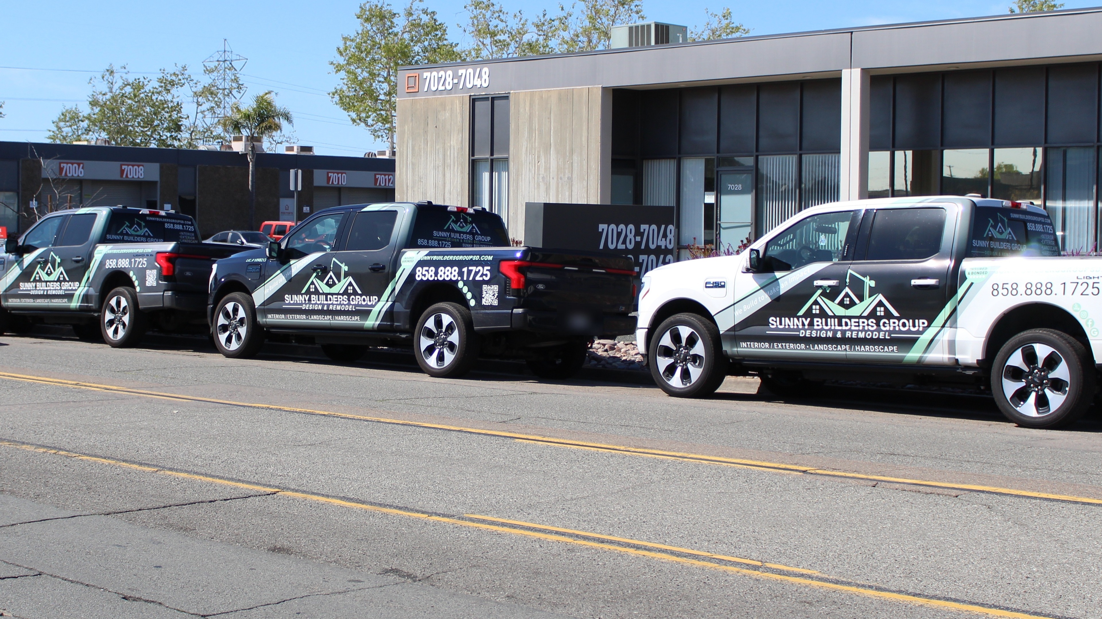Four wrapped Sunny Builders Group electric pickup trucks lined up outside the company office