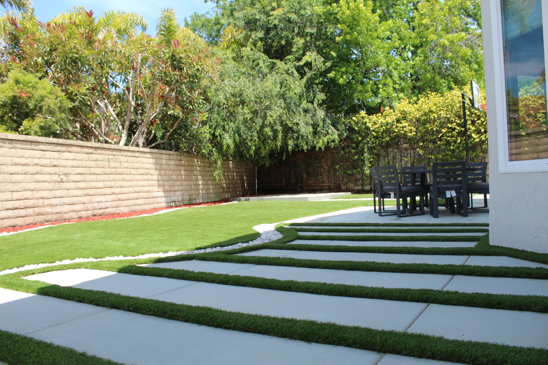 Concrete plank walkway with artificial turf joints and a white pebble ribbon edging the turf lawn