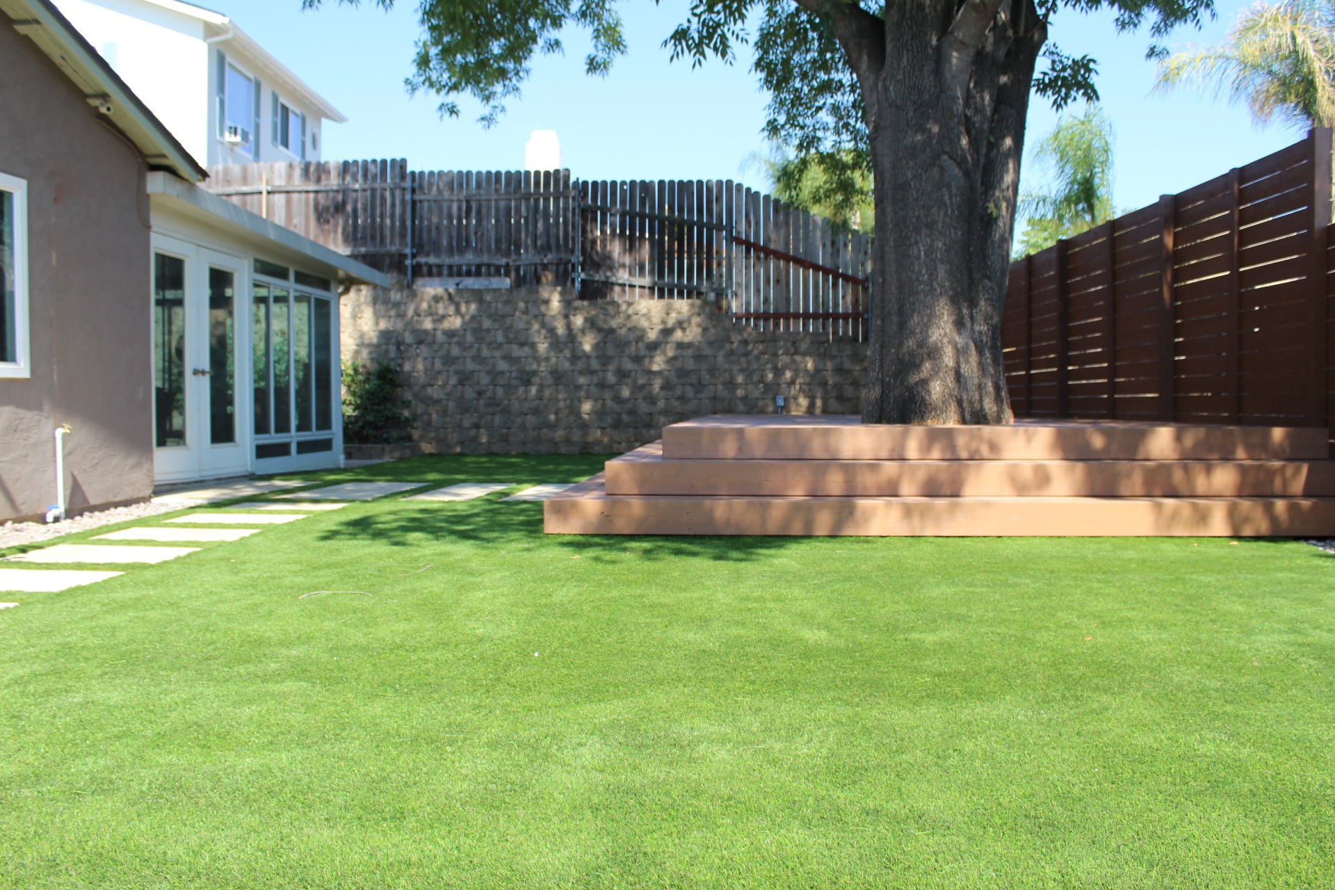 Seamless artificial turf lawn with a stepper path leading to a low floating deck and french doors