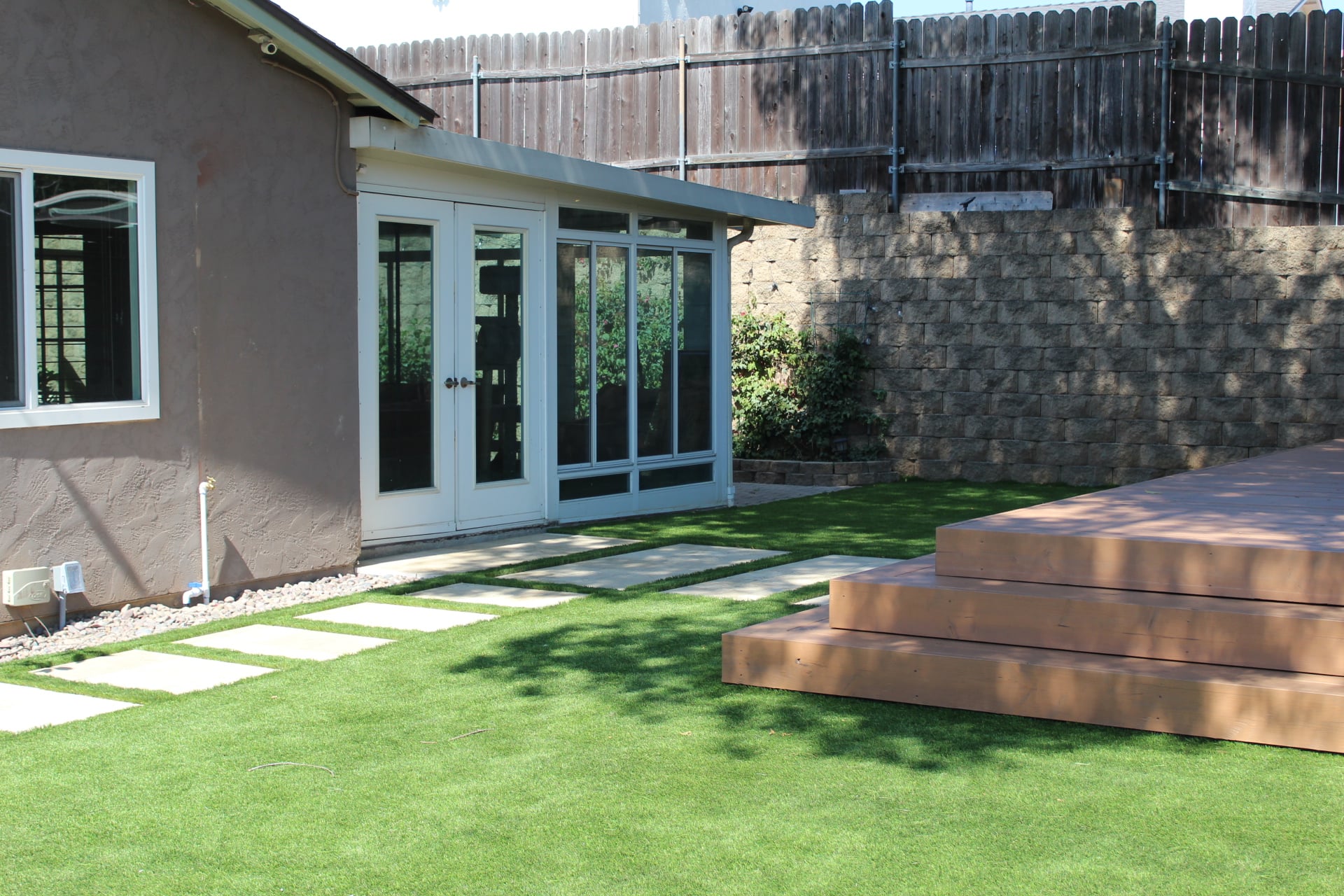 Backyard remodel seen from the folding glass doors, with a stepper walk, turf lawn and deck
