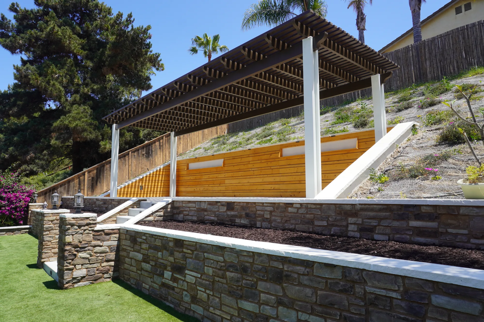 Chula Vista backyard remodel with a turf lawn, stone retaining wall, cedar screen and cantilevered patio cover