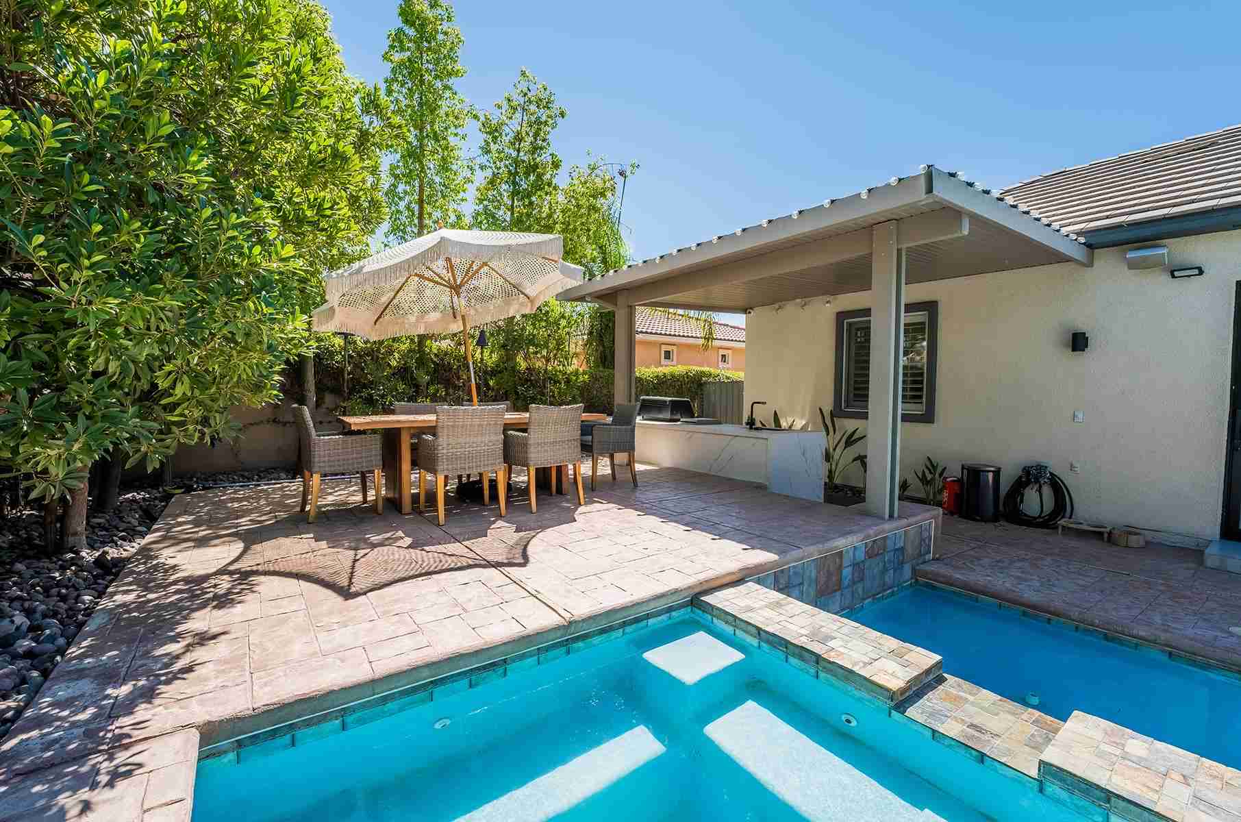 Pool and raised spa with stamped concrete patio, covered outdoor kitchen and shaded dining set
