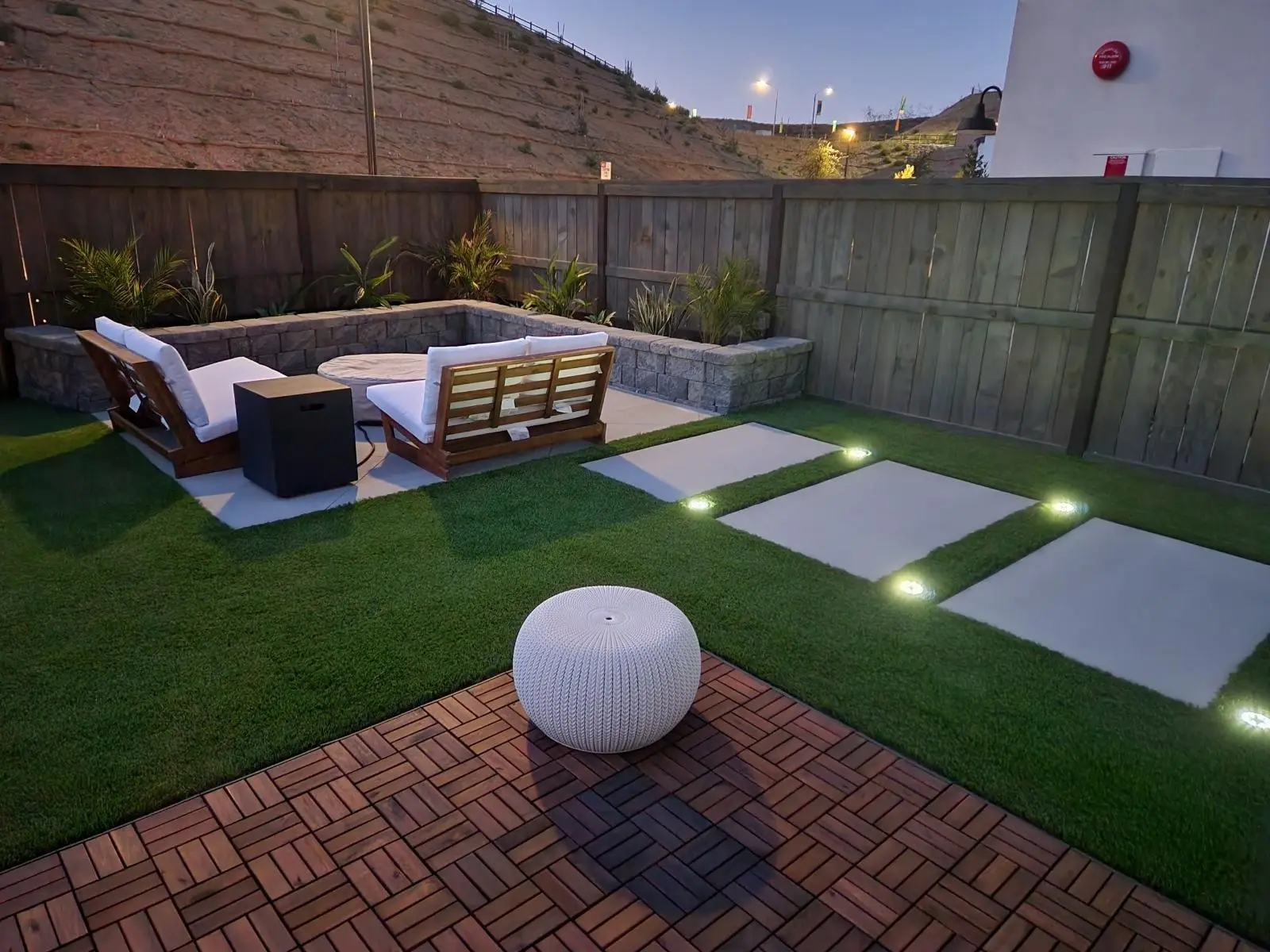 Backyard at dusk with artificial turf, lighted concrete pads, paver tiles and a lounge seating area