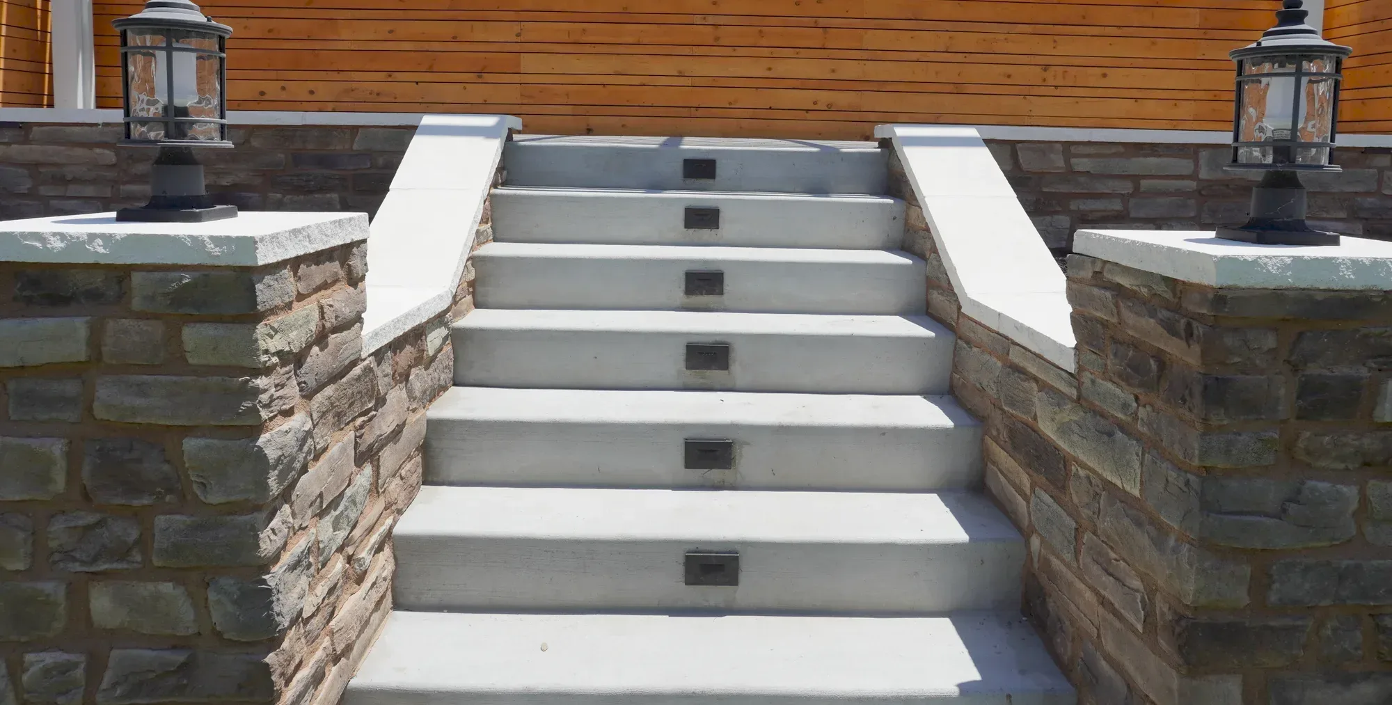 Poured concrete stairs rising between stone-veneer pilasters with lantern caps in Chula Vista