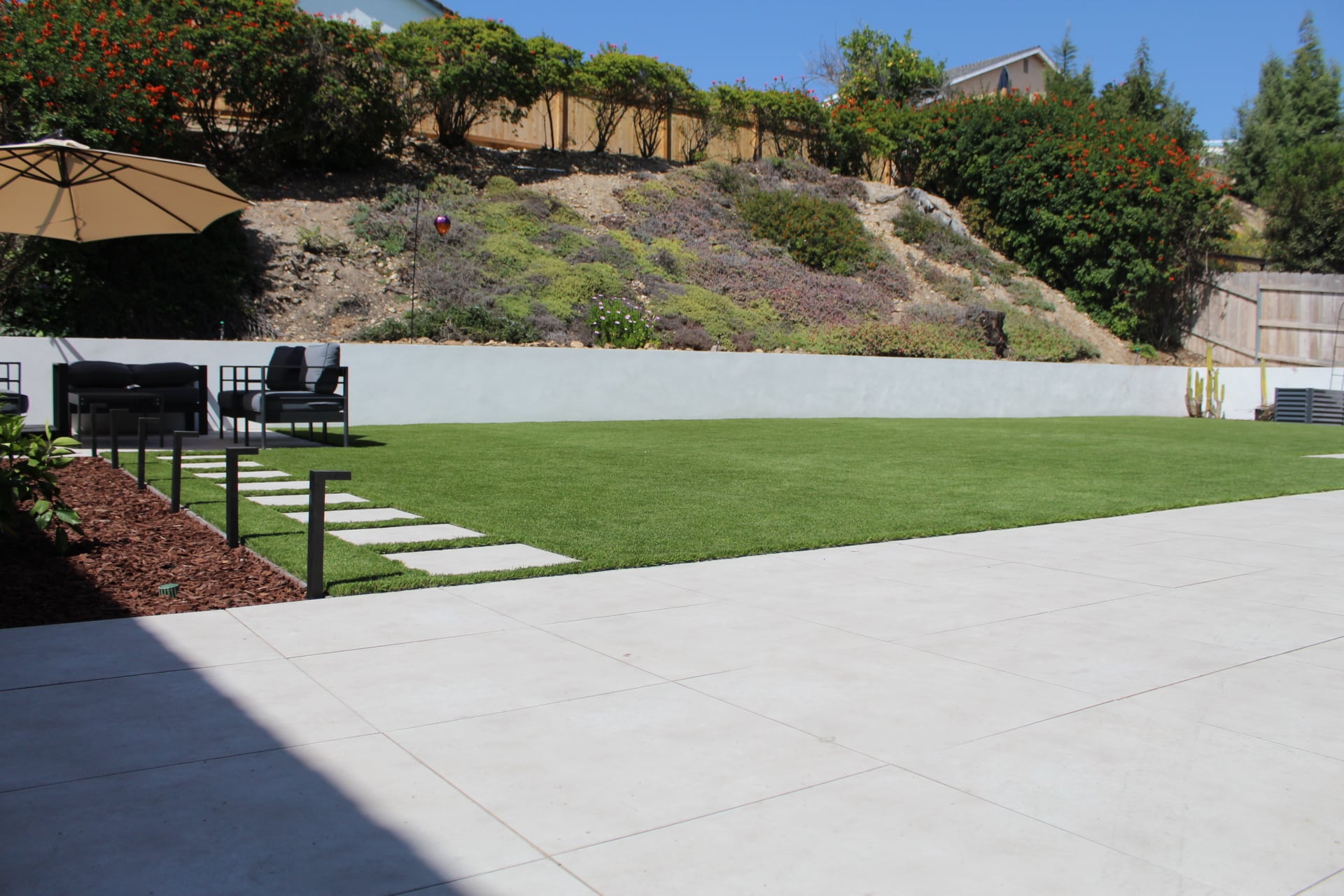 Saw-cut large-format concrete patio, turf edge, white slope wall and stepper path in Scripps Ranch