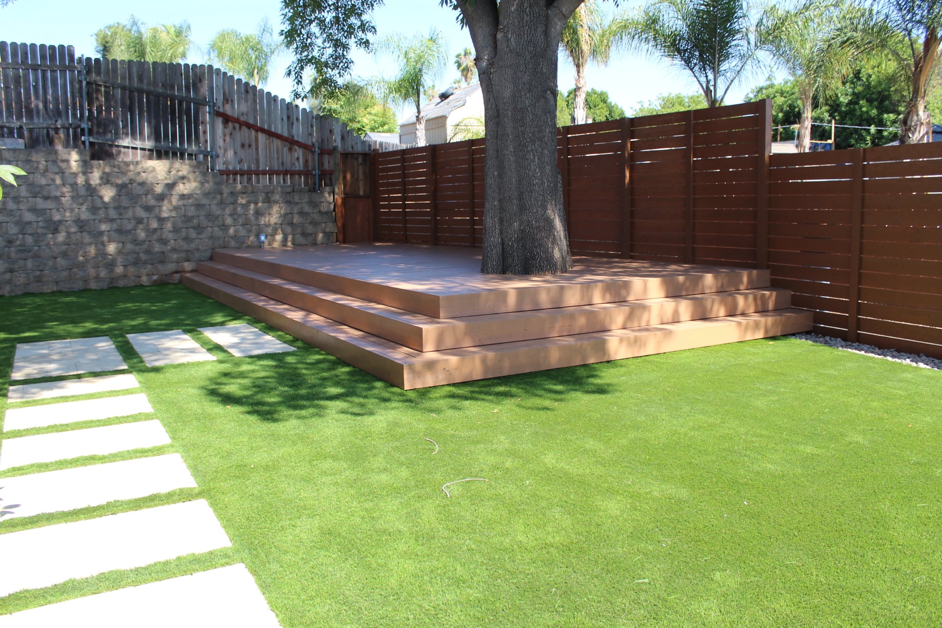Floating deck built around a mature tree with wrapping steps, a slat privacy screen and a turf lawn