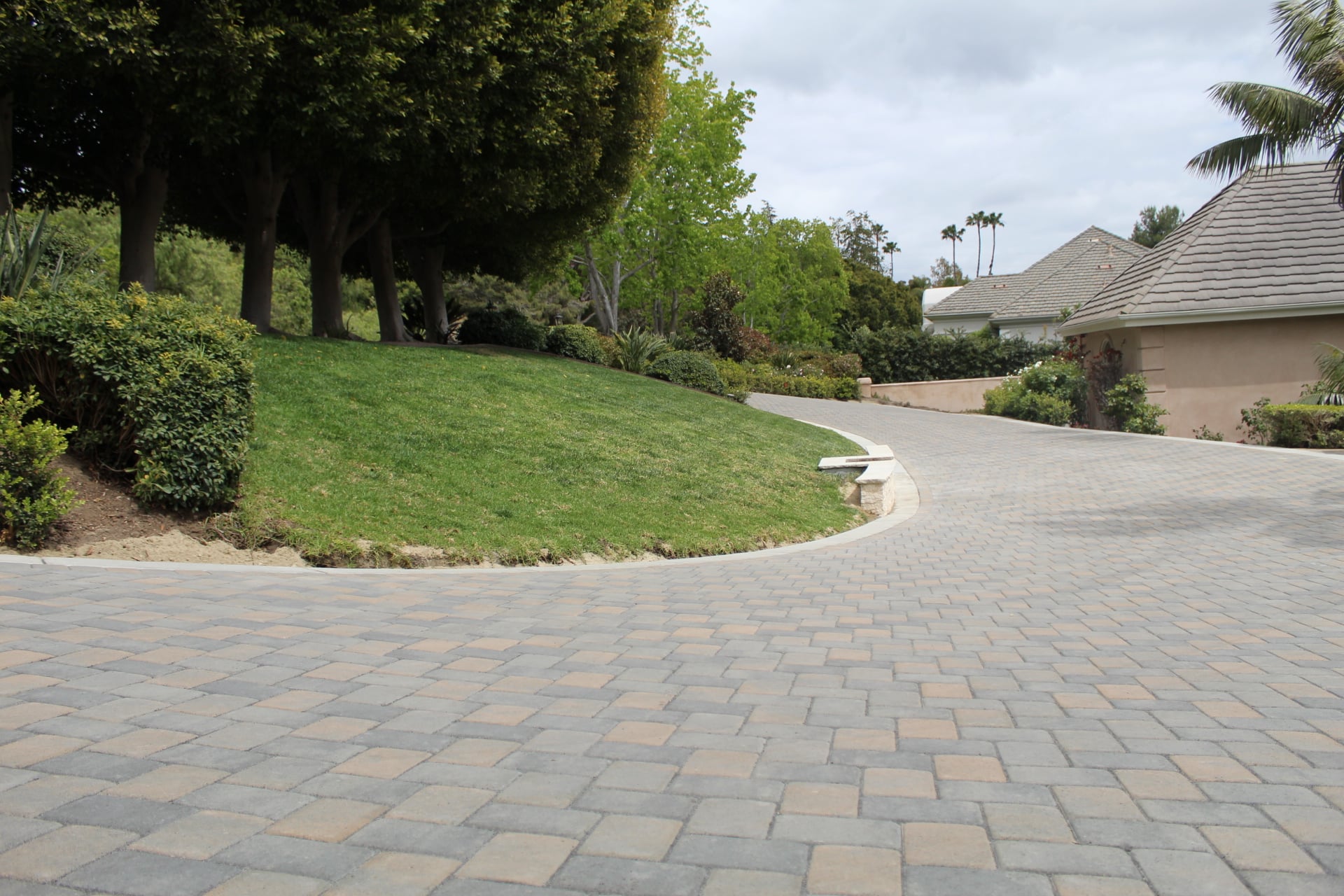 S-curve of a paver driveway past a banked lawn under an oak canopy