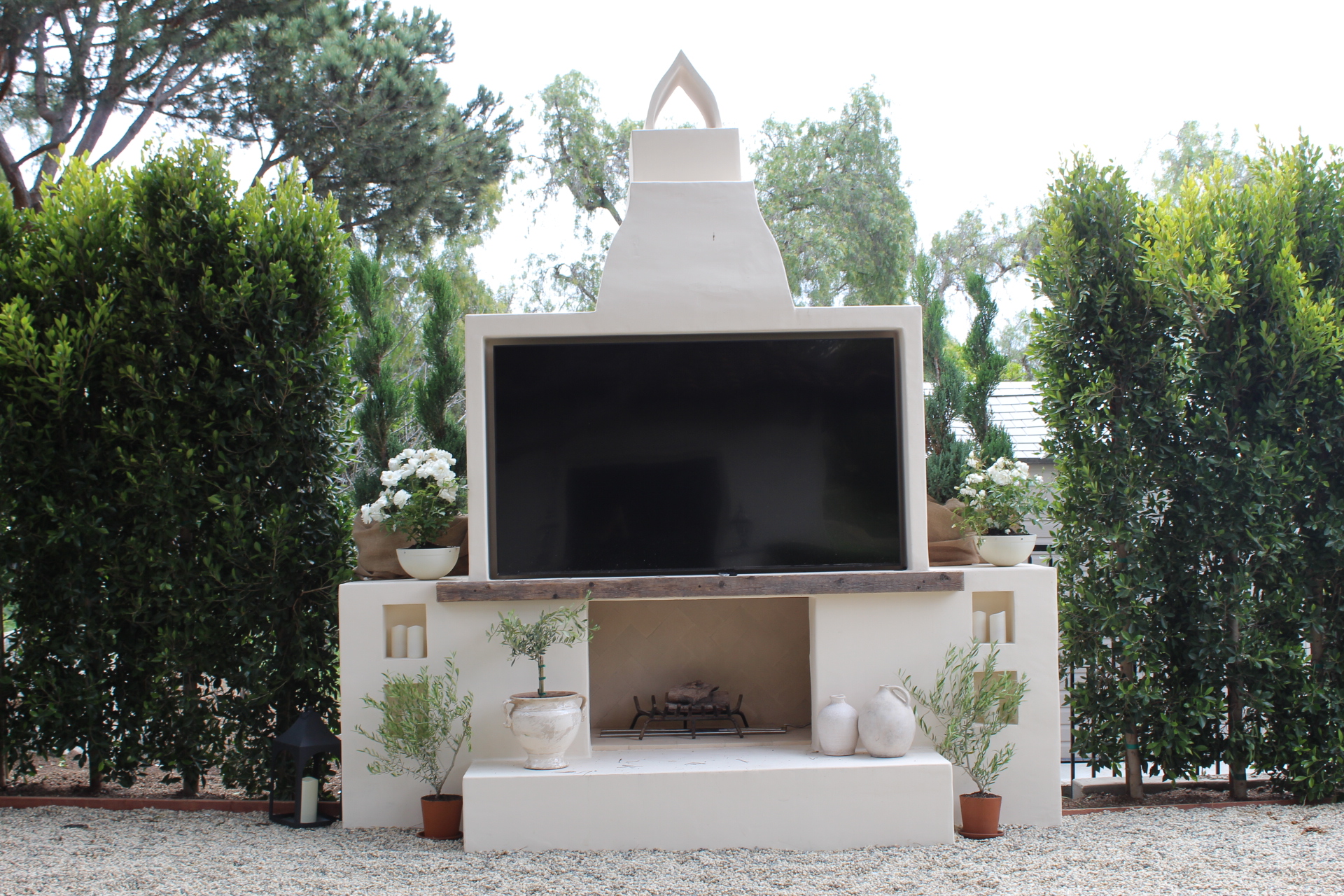 Rancho Santa Fe outdoor fireplace with a hearth bench, upper screen niche and potted olives on a gravel court