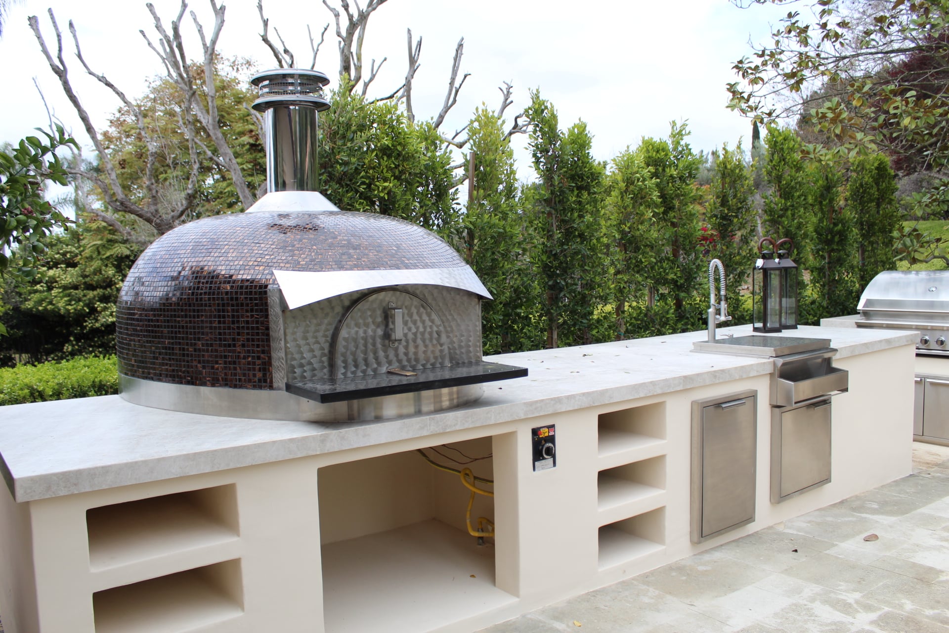 Mosaic-tiled pizza oven finished, with a citrus tree in a terracotta urn beside it in Rancho Santa Fe