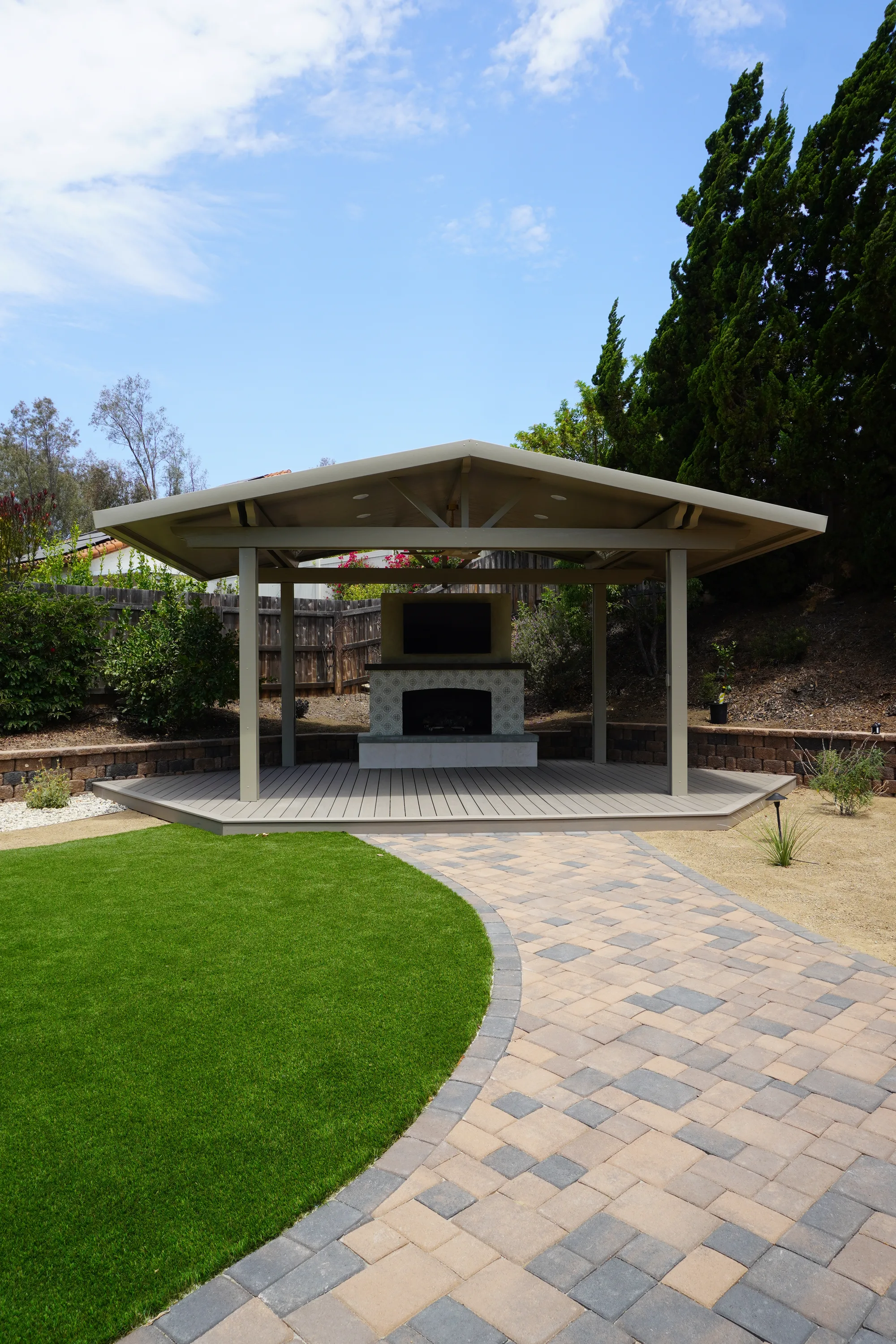 Gable pavilion on a composite deck with a tiled outdoor fireplace, curved paver patio and turf lawn in Poway