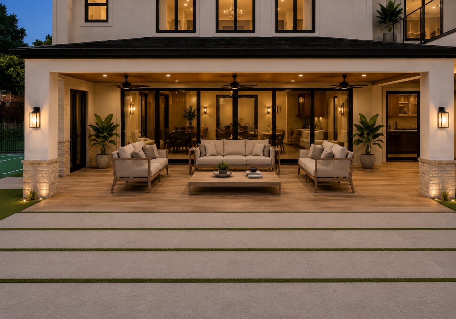 3D design rendering of a covered patio lounge at dusk with ceiling fans, stone-wrapped piers and porcelain paving with turf joints