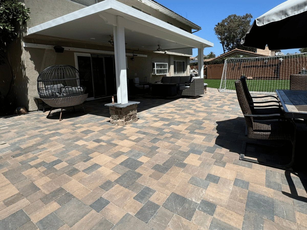 Tan and gray paver patio under a white patio cover with outdoor seating and a turf lawn beyond