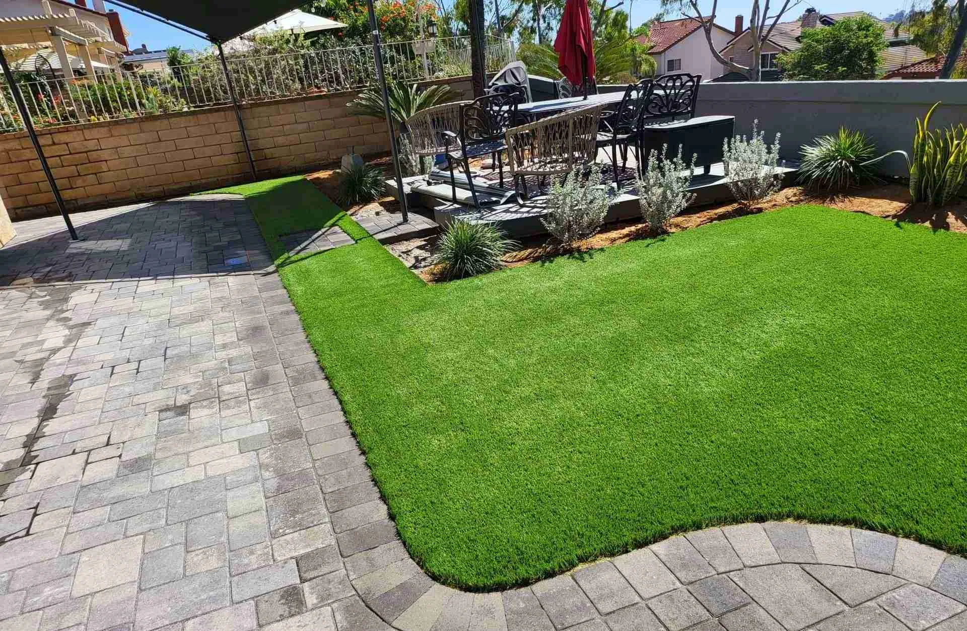 Artificial turf lawn framed by a paver patio and planting beds in a San Diego backyard