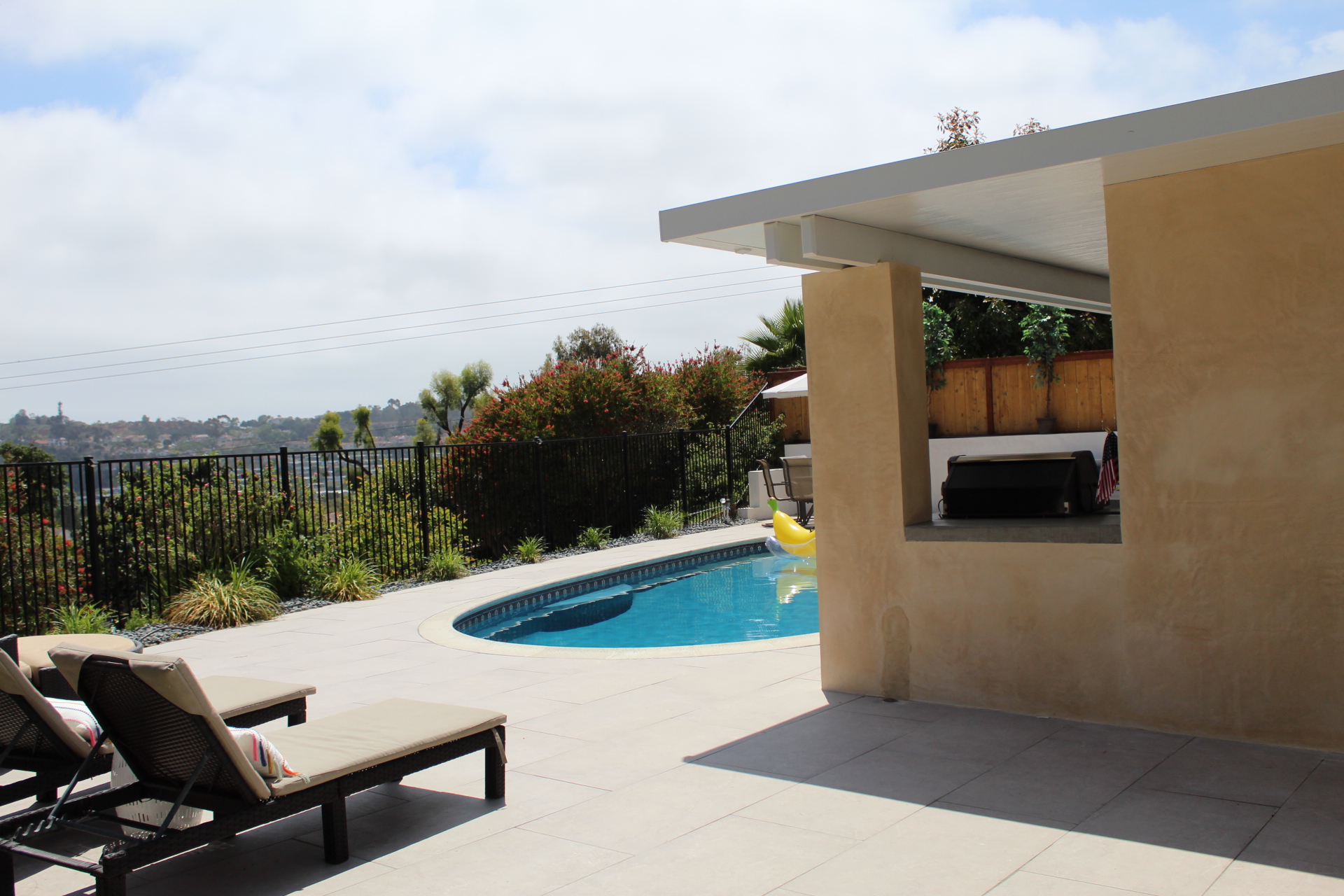 Chaise loungers on large-format pool decking beside a curving pool with an open valley view in Encinitas