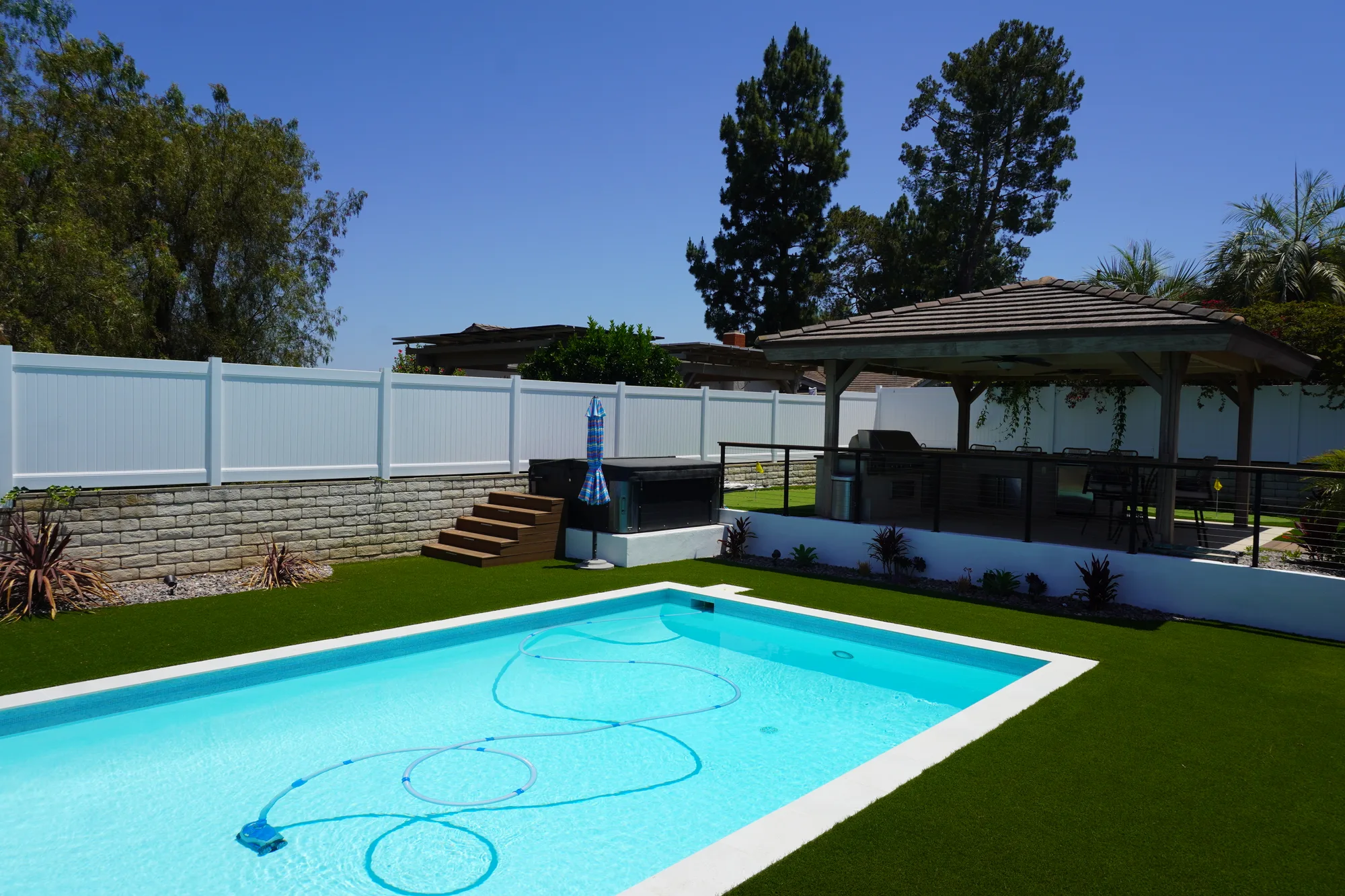 Rectangular pool and spa with turf running to the coping, beside a timber pergola with a built-in barbecue