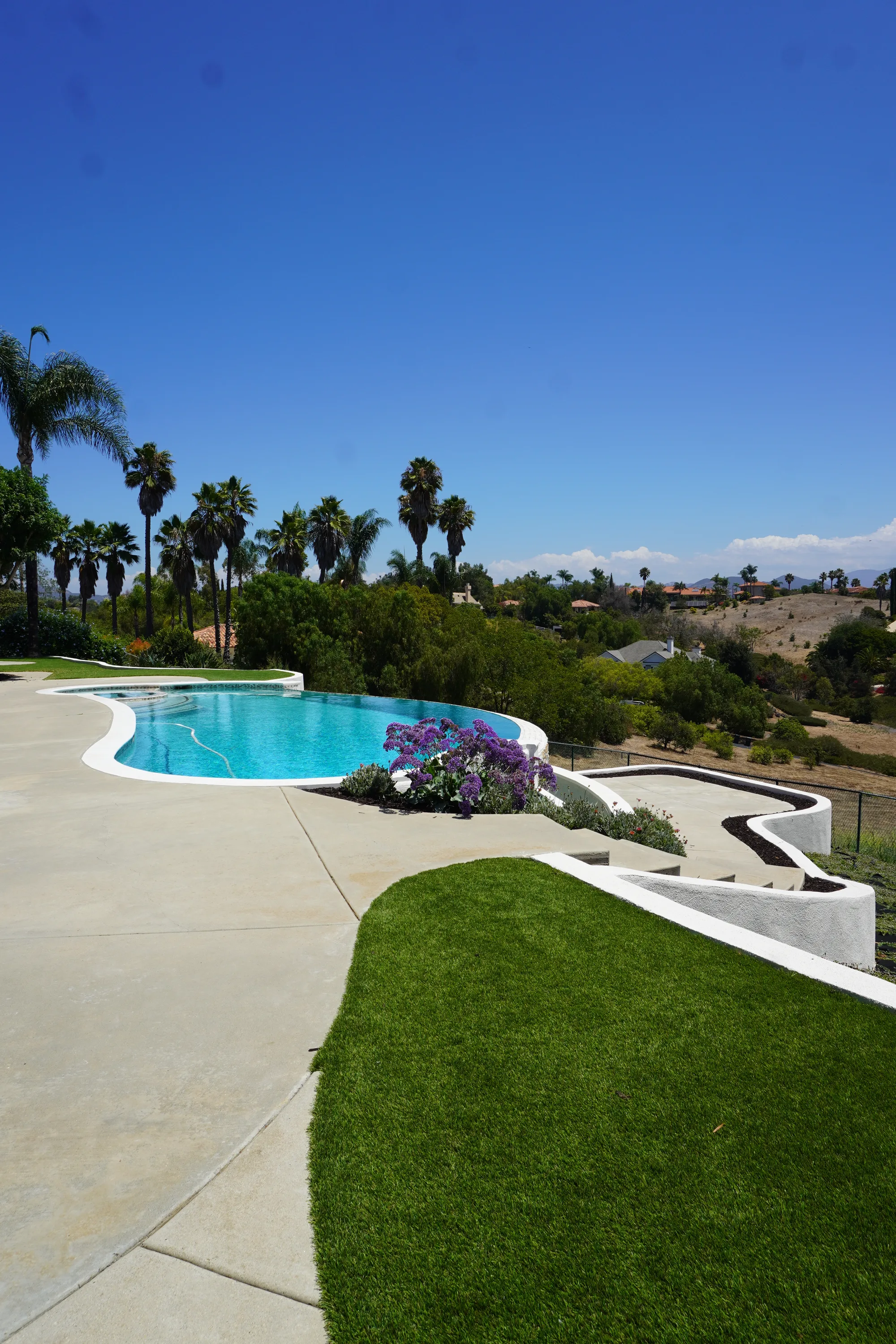 Hilltop Fallbrook pool with a broad concrete deck, turf lawn and serpentine white planter walls stepping down the slope