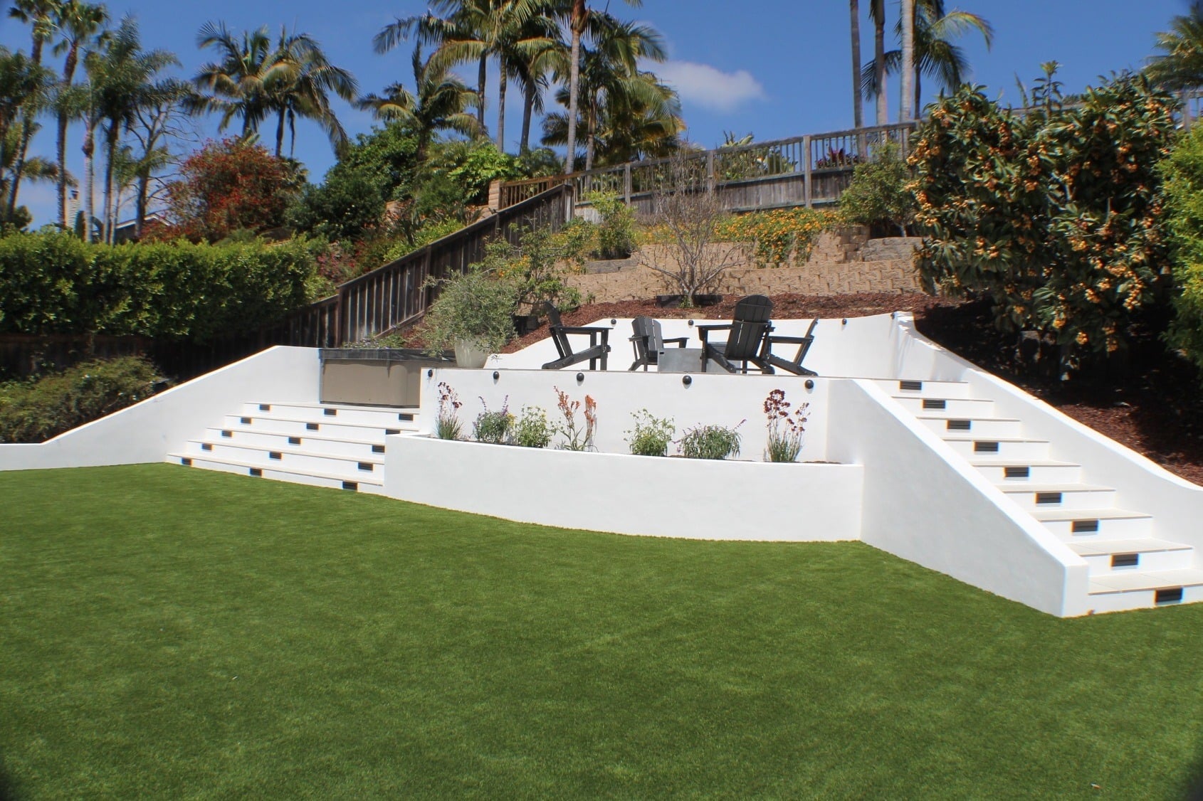Terraced white retaining walls with lit steps above an artificial-turf lawn on a hillside lot