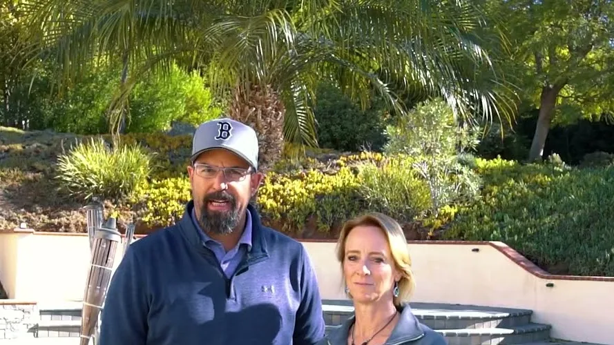 Homeowners on camera beside the pool terrace and planted slope at a Poway backyard project