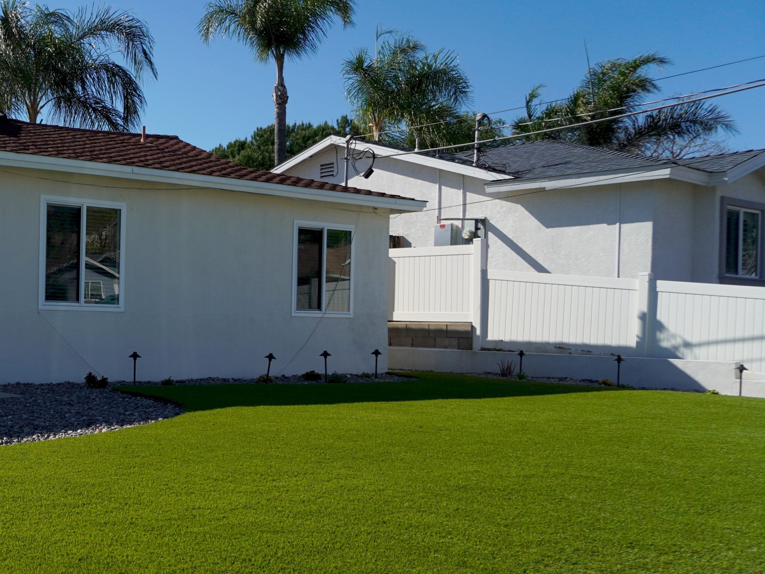Artificial turf front lawn sweeping past two white single-story San Diego homes