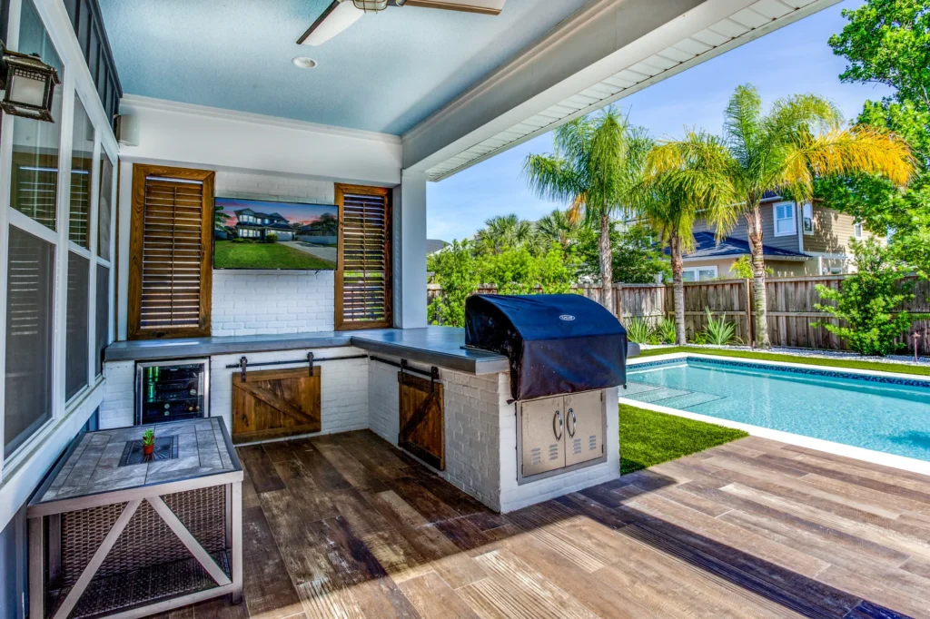 Covered outdoor kitchen with built-in grill beside a backyard pool