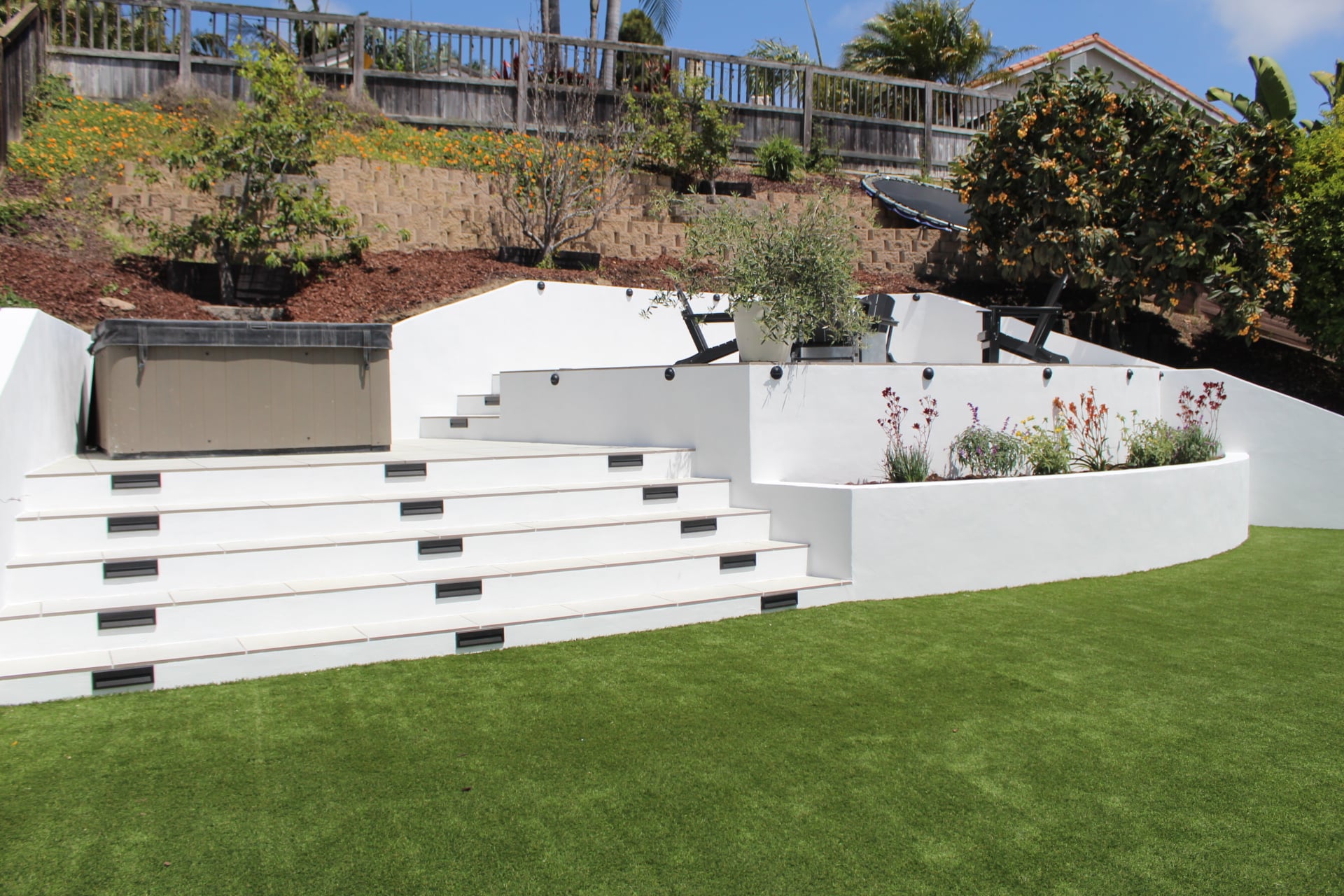 White terraced retaining walls with built-in stairs above a turf lawn on a hillside