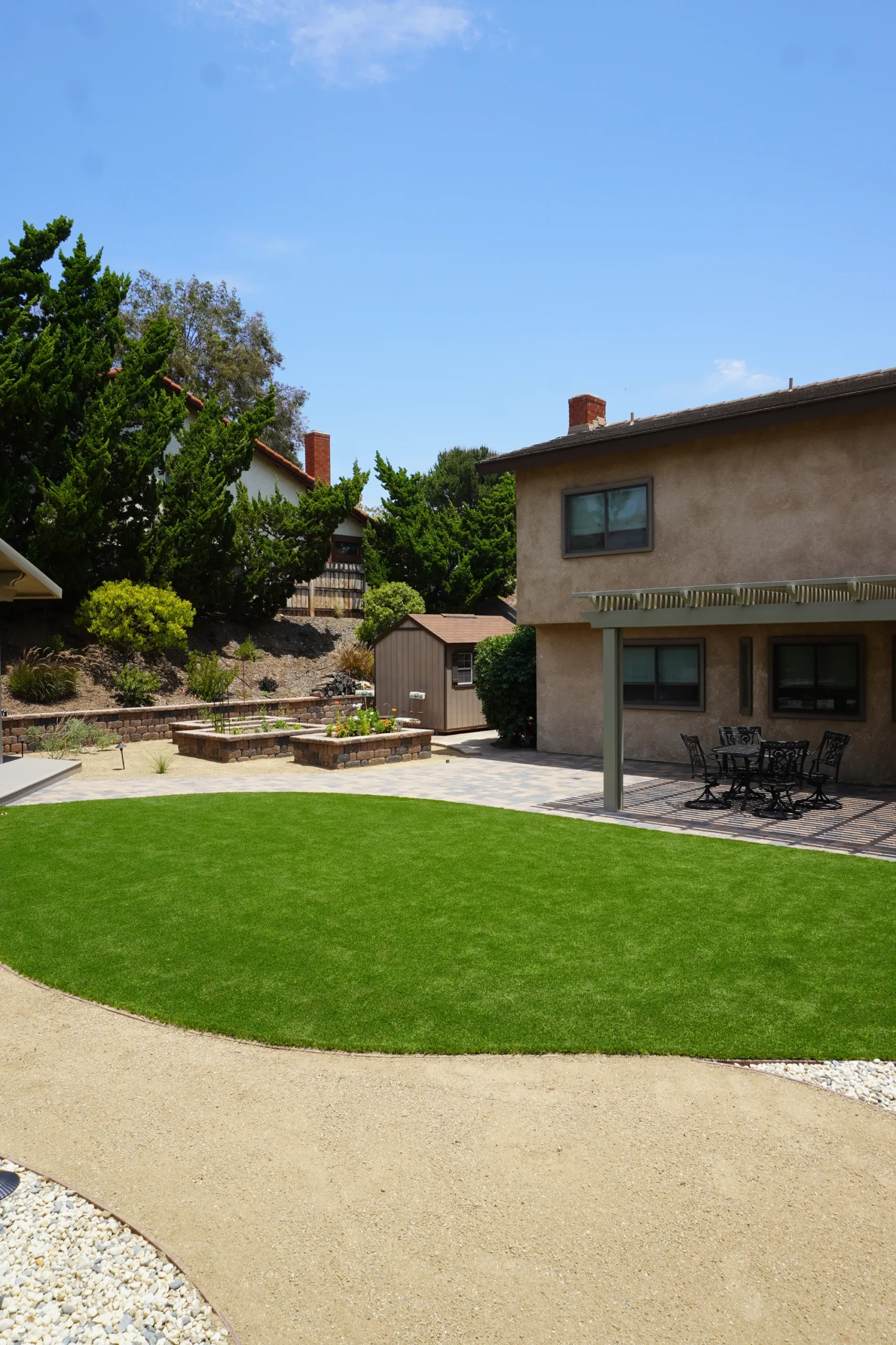 Finished Poway backyard with a curved turf lawn, decomposed granite path, raised paver garden beds and a covered paver patio dining area below a planted slope